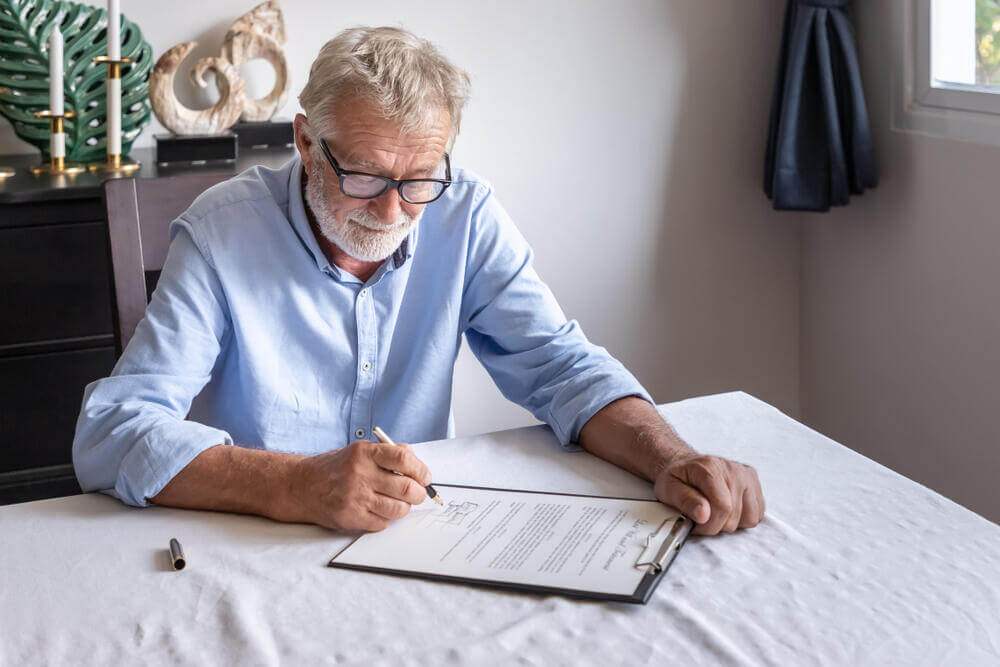 Relaxed senior man signing a legal document at home for his estate plan