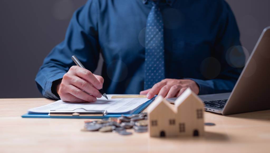 A man in a tie signing documents on a clipboard.