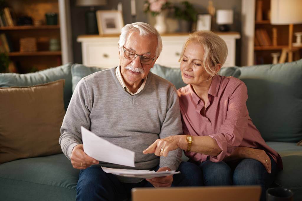 A senior couple sitting on a couch and looking at paperwork.